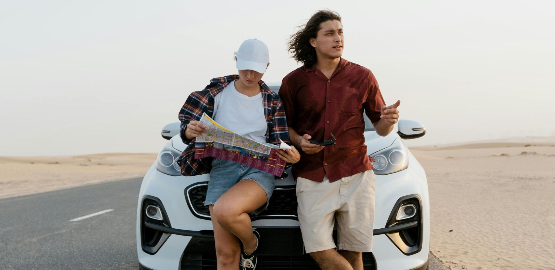 A couple reviews a map while standing next to their car in a desert. Perfect for travel and adventure themes.